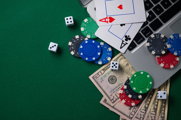 Online poker chips and dice near the keyboard on the gaming green table.