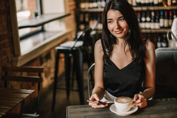 Woman using phone and drinking coffee in a cafe.