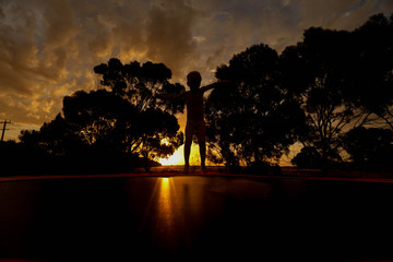 Child silhouette jumping on trampoline at sunset 