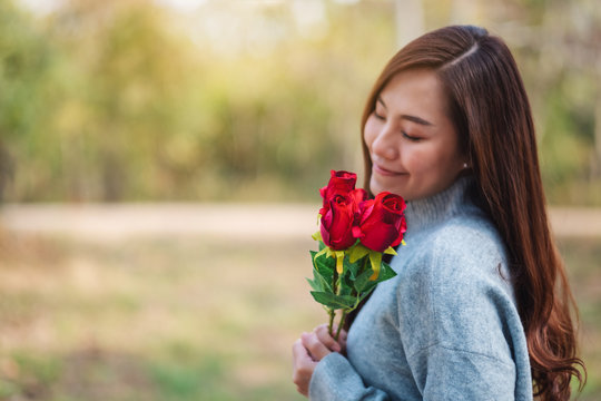 Closeup image of a beautiful asian woman holding and smelling red roses flower with feeling happy on Valentine's day
