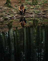 Green moss on the rocks in the forest during rainy day with a male photographer / forest reflection in water pond