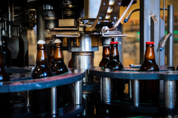 Beer bottles in factory during process of placing caps on top (high ISO image)