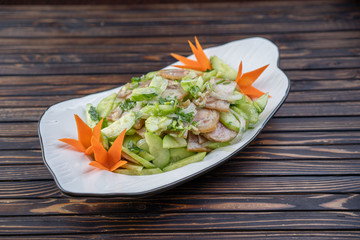 Typical Chinese salad of cucumbers and pork in a white plate on a wooden background