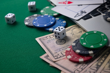 Online poker chips and dice near the keyboard on the gaming green table.