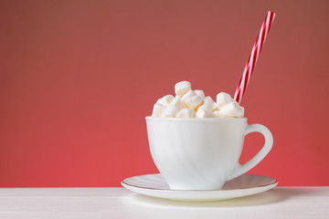Marshmallow in a white Cup on a white table on a pink background.