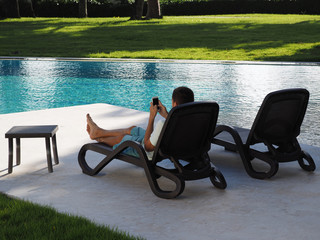 Relax in the hotel with a phone in hand. A man lying on a lounger by the pool and using smartphone....