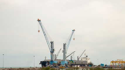 Fototapeta na wymiar Large cargo cranes and large cargo ships dock at the harbor.