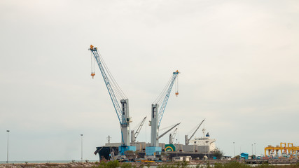 Fototapeta premium Large cargo cranes and large cargo ships dock at the harbor.