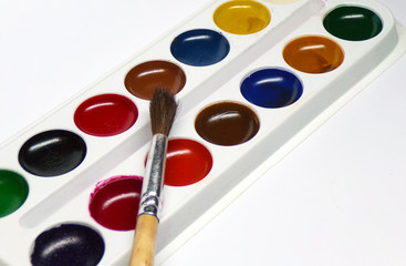 Watercolor paints with a brush. School supplies. Palette of colors of watercolor paint. Artist's tools.