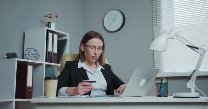 Business Woman Shopping Online with Laptop in Office. Young Woman Hold Bank Credit Card in Hand and Buying From Computer.