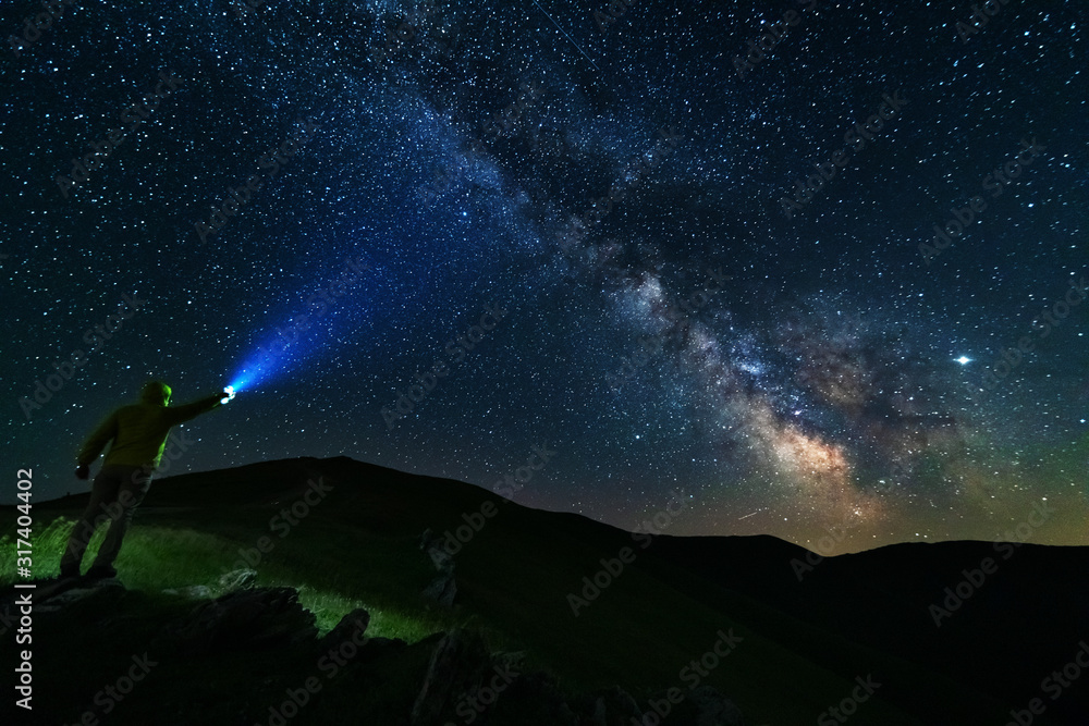 Wall mural bright starry sky with the milky way on the background of mountains and hiker with red tent.