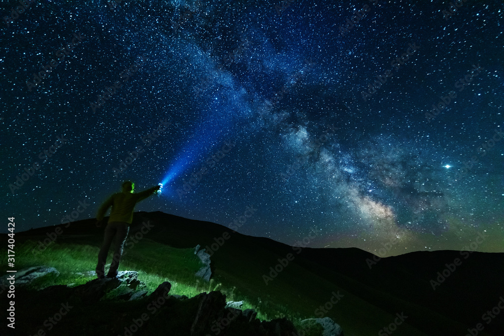 Wall mural bright starry sky with the milky way on the background of mountains and hiker with red tent.