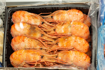 Frozen boiled shrimp are in a cardboard box. Shrimps are laid in two rows.