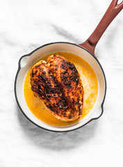 Simple roasted chicken breast in a cast iron pan on a light background, top view