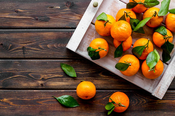 Tangerines with leaves on tray - as fruit harvest - on dark wooden background top-down copy space