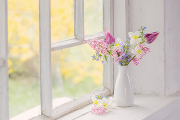 spring flowers in white vase on old windowsill