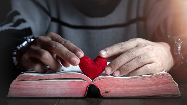 Hands and Red heart in bible on wooden table in morning, Close up, love of christian concept.