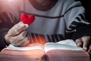 Holding Red heart in hand with Bible on wooden table, Close up, love of christian concept.