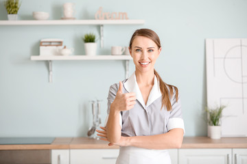 Portrait of beautiful chambermaid showing thumb-up in kitchen