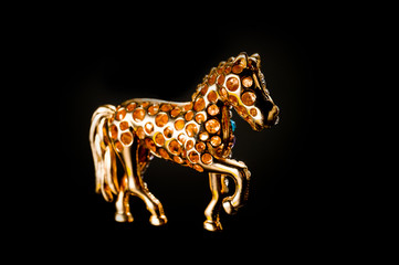 Horse figurine souvenir keychain in gold color ornate with bright pebbles shot on a dark background