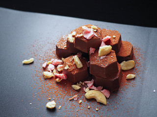  piled up chocolate with top of crushed hazelnuts, pink chocolate pieces and cocoa powder on dark background.
