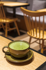 hot green tea contains in a dark color mug with a small plate placed on a wooden table with cafe environment