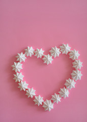 Meringue kisses in heart shape on pink background