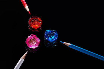 colored pencils and plexiglass flowers on a black background with reflections
