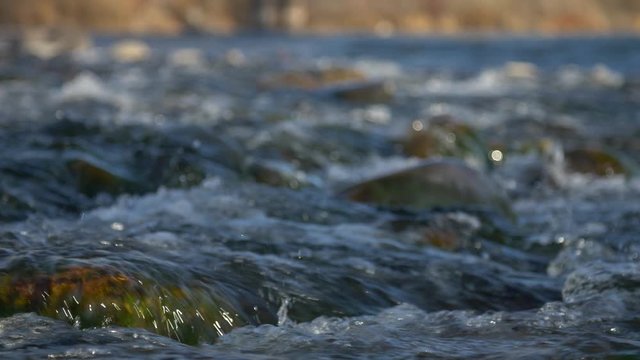 Low angle slow motion slider shot pushing in over small river rapids at golden hour.  Focus near frame.