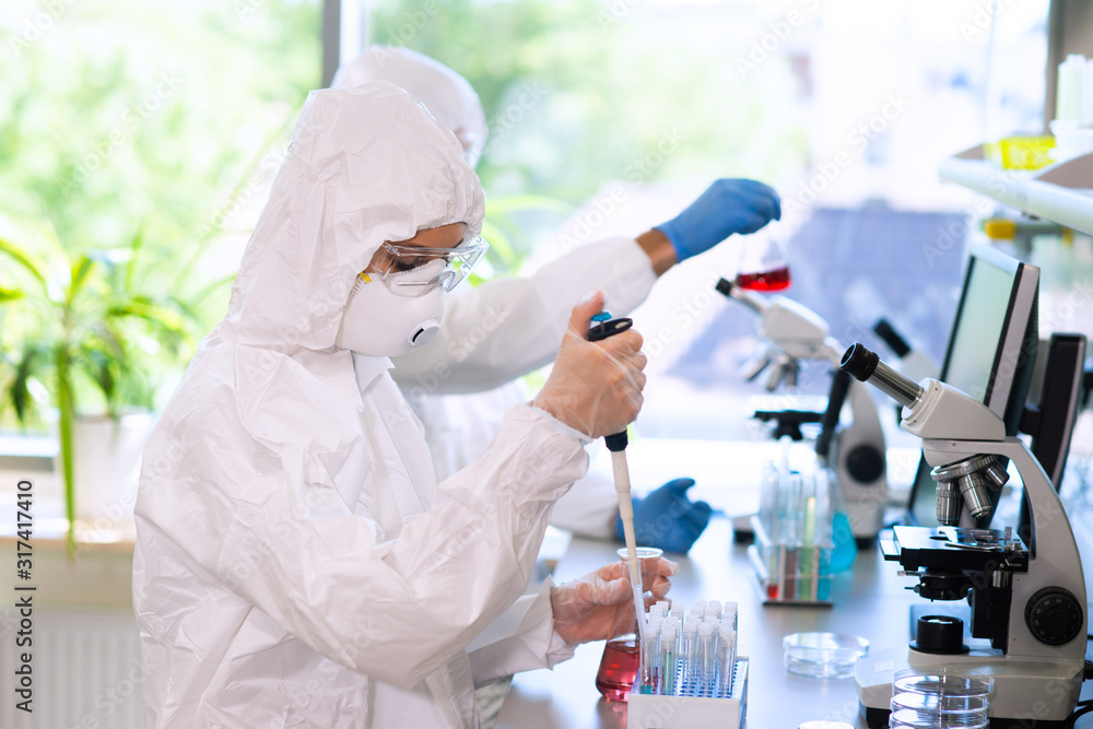 Wall mural scientists in protection suits and masks working in research lab using laboratory equipment: microsc