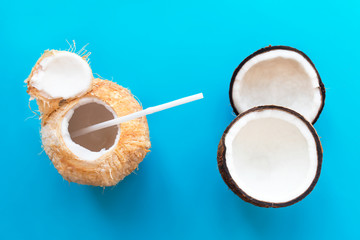 Coconut benefits, set, composition of fresh coconut cut in half, two halves, cocktail coconut juice, milk, water with straw. Top view on blue background. Healthy natural food