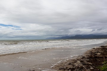shore of the beach with fog and rain-laden clouds between the mountains in front of the beach and a lot of vegetation. Port Douglas