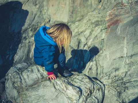 Little toddler climbing on rocks in winter
