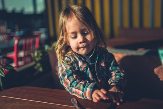 Little toddler sitting at cafe table with cutlery