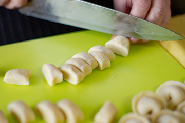 Someone's hands are slicing the dough for dumplings with a kitchen knife.