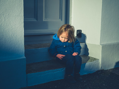 Little toddler sitting on steps outside house in winter