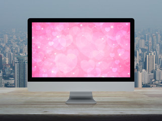 Desktop modern computer monitor with pink love heart screen on wooden table over office building tower and skyscraper in city, Business internet dating online, Valentines day concept