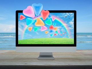 Colorful love heart balloon, green grass field, sky, rainbow and birds with desktop modern computer on wooden table over tropical sea and blue sky with white clouds, Business internet dating online, V