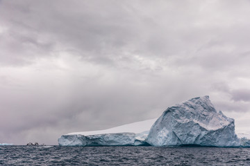 Iceberg floating in the cold water of Antarctica in front of snowy mountains
