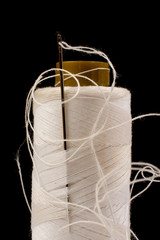 Needle and white cotton, tangled yarn on roll for sewing. Thread used in fabric and textile industry. Black background