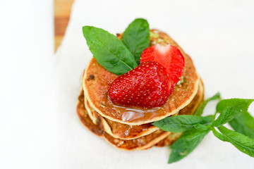 Pile of golden pancakes with strawberries and decorative sprig of mint. Close-up