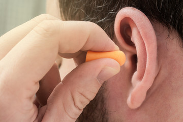 Man putting ear plugs into ears to protect hearing and get rid of noise. Concept for World Hearing...
