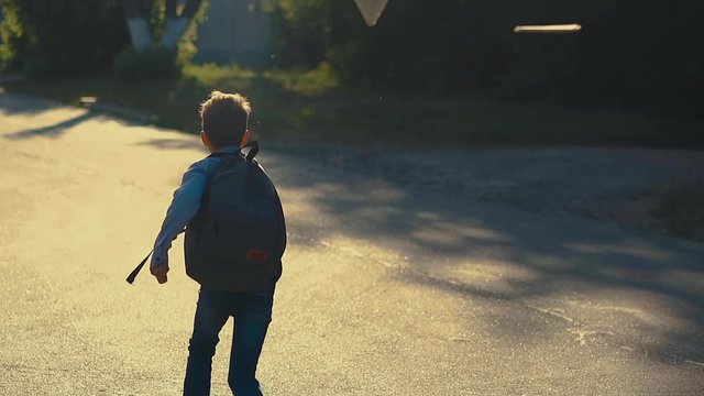 young student guy with schoolbag jumps on grey asphalt road and throws up sheets when skips school slow motion backside view