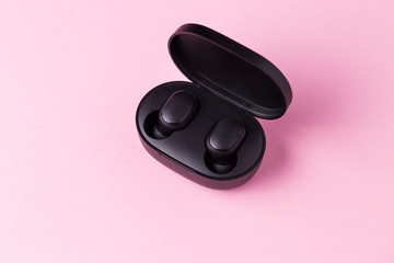 Close-up black wireless headphones on pink isolated background.