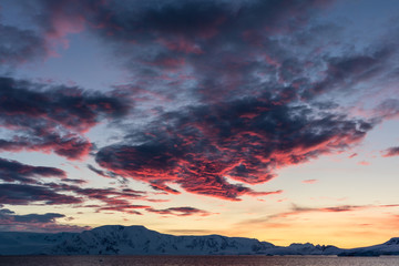 Fototapeta na wymiar Pink clouds at sunset over the mountains and water of Antarctica, a pristine remote landscape