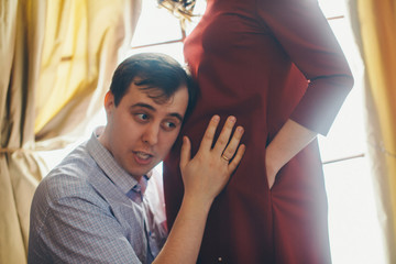 a loving couple embraces at the window. A man and a woman look into each other's eyes. The husband hugs his pregnant wife and strokes her stomach. Valentine's day. February 14