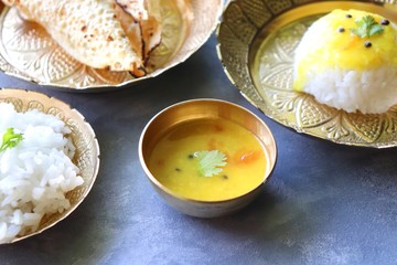 Healthy Indian comfort food Dal Chawal thali or Dal Rice. Served in copper vessels with buttermilk, glass of water and roasted papad or papadam. Over moody royal background with copy space.