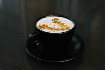 black cup of cappuccino with a saucer on a table with a pattern of cinnamon