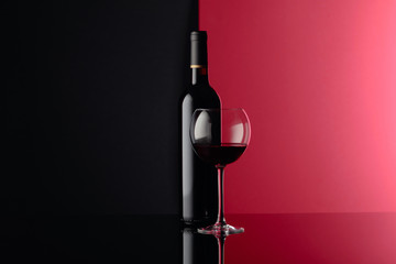 Glass and bottle of red wine on a black reflective background. Copy space.