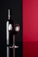 Glass and bottle of red wine on a black reflective background. Copy space.